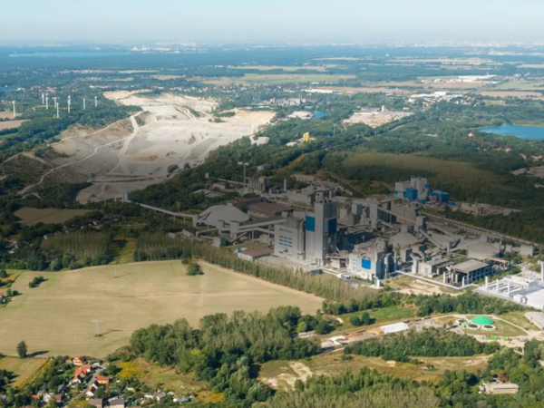 Panoramic view of the Rüdersdorf cement plant with quarry, green landscape, and lakes in the background. The image symbolizes sustainable industry in harmony with nature.