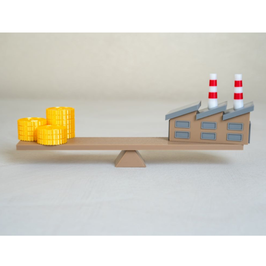 Symbolbild einer Waage mit einer Fabrik auf der einen Seite und Geldmünzen auf der anderen, das den wirtschaftlichen Ausgleich zwischen Industrie und Kosten darstellt.