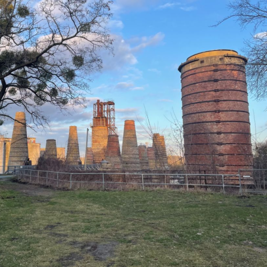 Außenaufnahme historischer Industrieöfen und Türme aus Ziegelstein in einem Freilichtmuseum, umgeben von Wiesen und Bäumen.