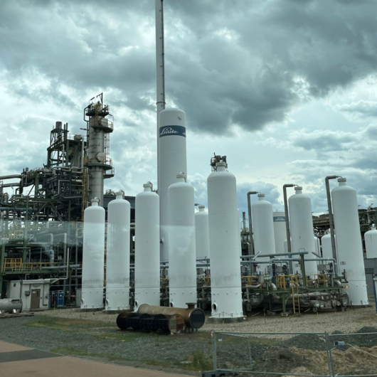 Modern industrial plant with large white tanks and pipelines under cloudy skies, part of a gas processing project.